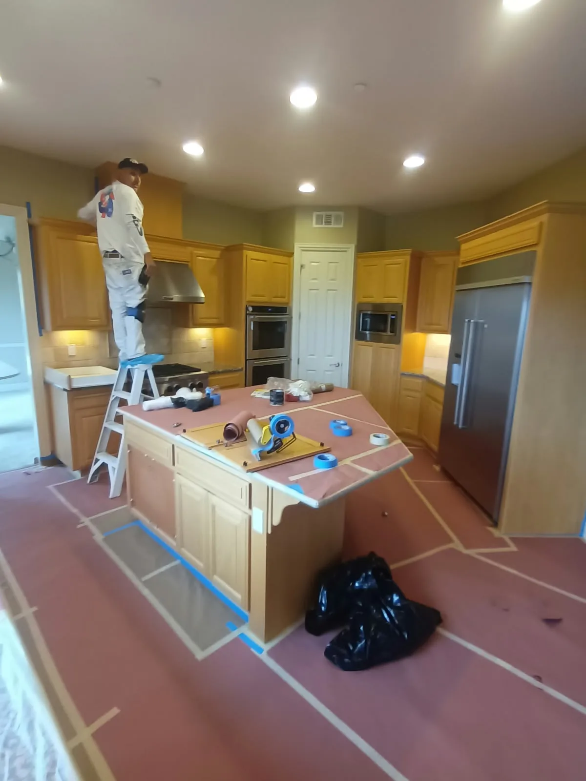 Interior painting in San Jose, CA: painter on a ladder in a kitchen with floors and counters masked