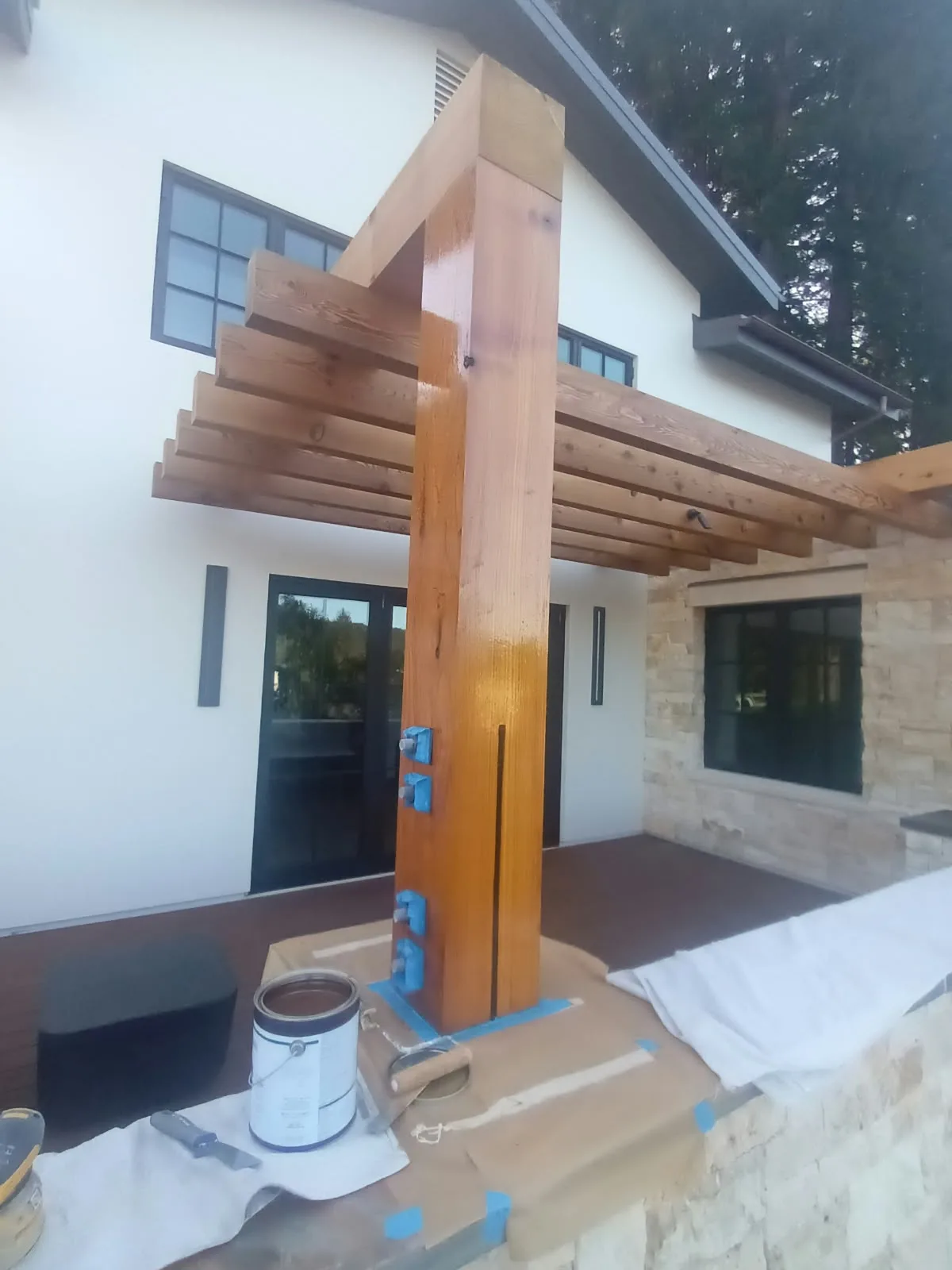 Wood refinishing in San Jose, CA: pergola post taped and prepped with a paint can beside it
