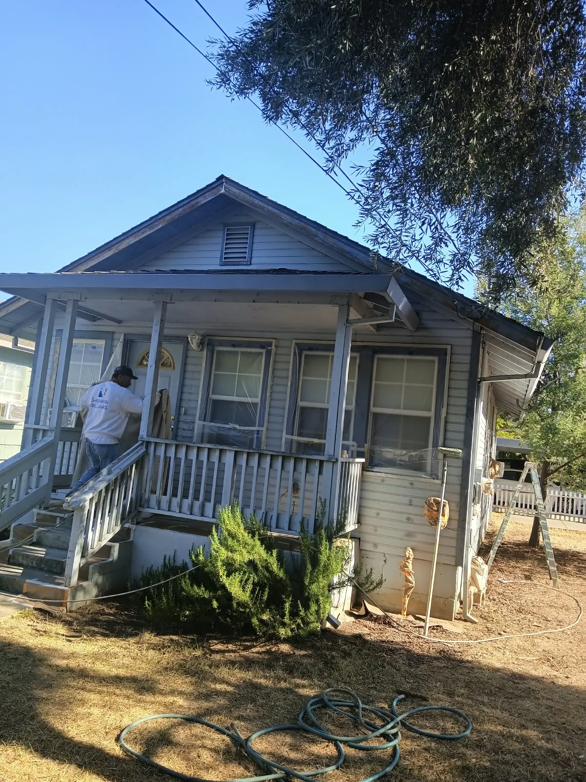 Exterior painting in San Jose, CA: painter working on the porch of a wood-sided house